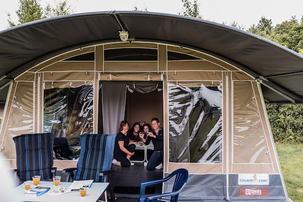 Un grand espace extérieur aménagé, abrité et doté de chaises à rayures bleues et d’une table où sont disposées des boissons et des documents.
