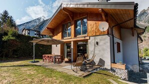 A modern house with a wooden deck, outdoor seating, and a mountain backdrop.