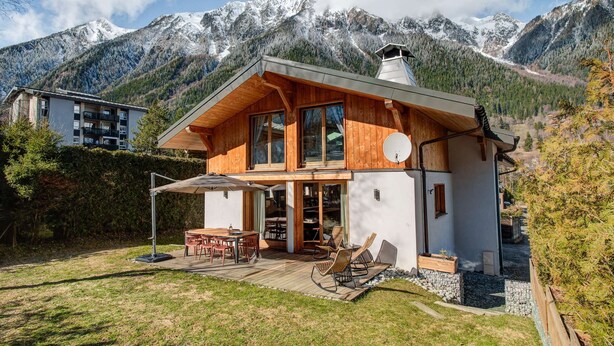 A wooden chalet with a deck, a dining area, and a view of snow-capped mountains.