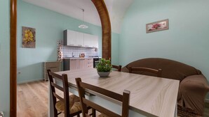 A dining area with a wooden table and chairs, a kitchen in the background, and a large arched doorway. - 3729 Pio Apartment by Barbarhouse (Lecce)