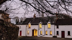 A traditional white building with multiple windows, a central entrance, and a stone wall on the left.