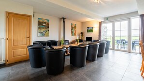 Um quarto amplo com porta de madeira, banquetas cilíndricas pretas, uma mesa de madeira e obras de arte nas paredes.