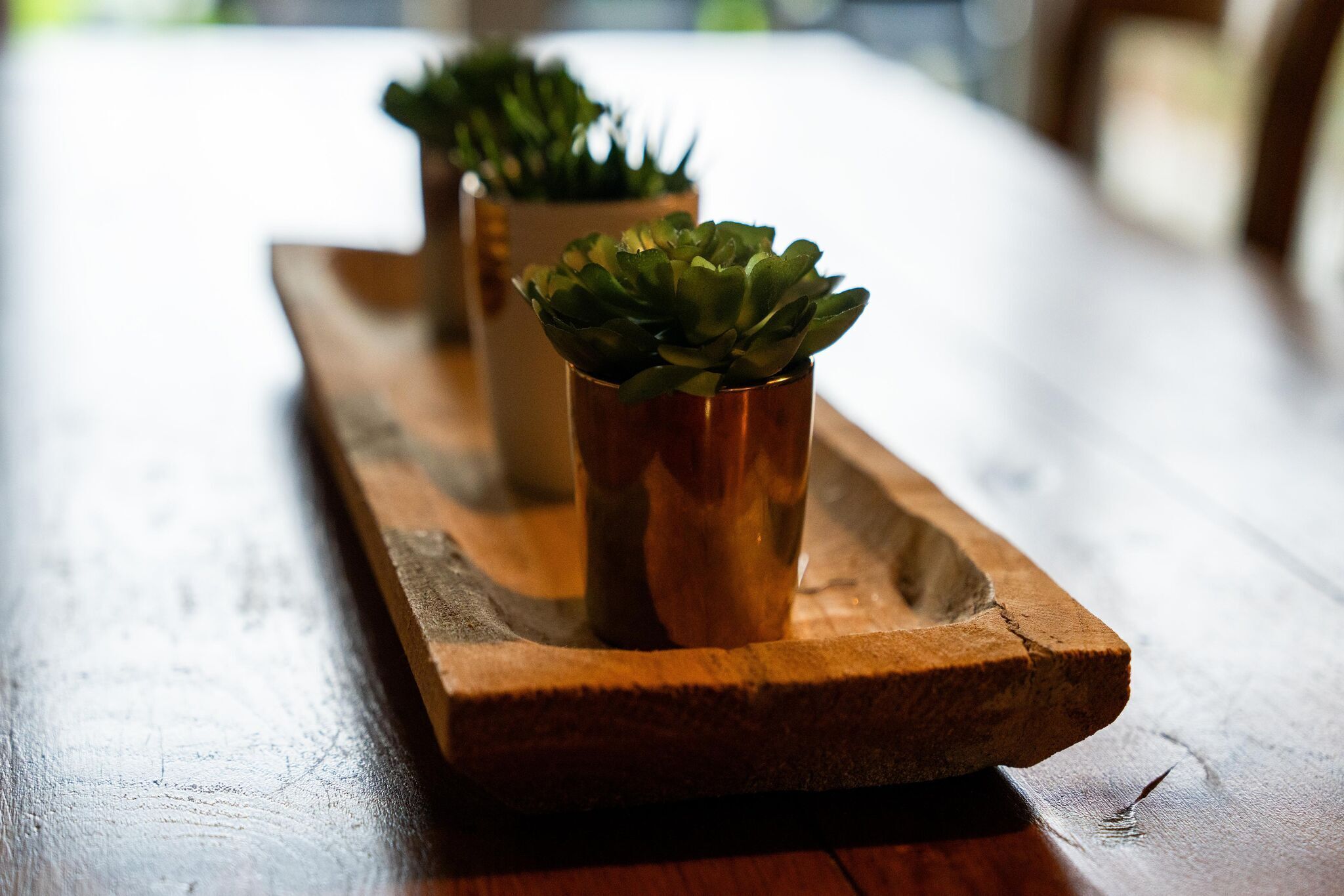 A wooden tray with two copper pots containing green plants.