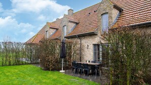 A stone house with a tiled roof, a patio with a table and chairs, and a grassy area. - Apartment on Belgium's Stunning Coastline (Diksmuide)