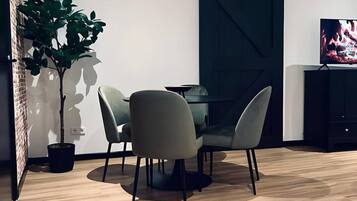 A modern dining area with a round table and four chairs, a potted plant, and a television on a cabinet.
