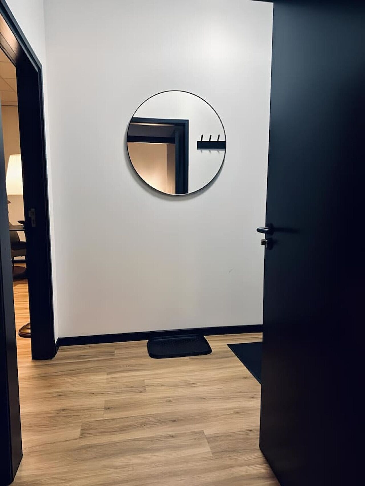 A modern room with a wooden floor, a round mirror on the wall, and a door.