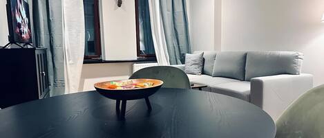 A modern living room with a round black table, a grey sofa, and a window with curtains.