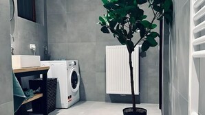 Une buanderie moderne équipée d’un lave-linge et d’un sèche-linge encastrés, d’une plante en pot et d’un radiateur.