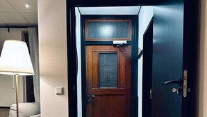 Un couloir avec une porte en bois, un lampadaire et un paillasson.