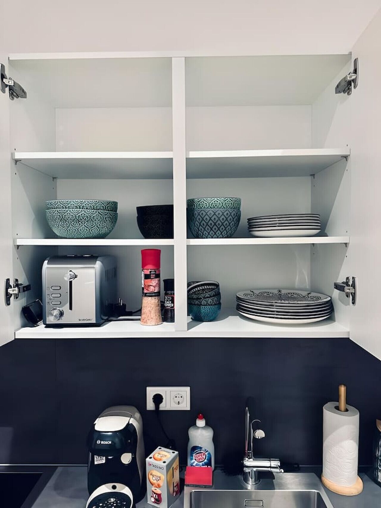 A kitchen with white cabinets, a Bosch coffee maker, a toaster, and various kitchen utensils.
