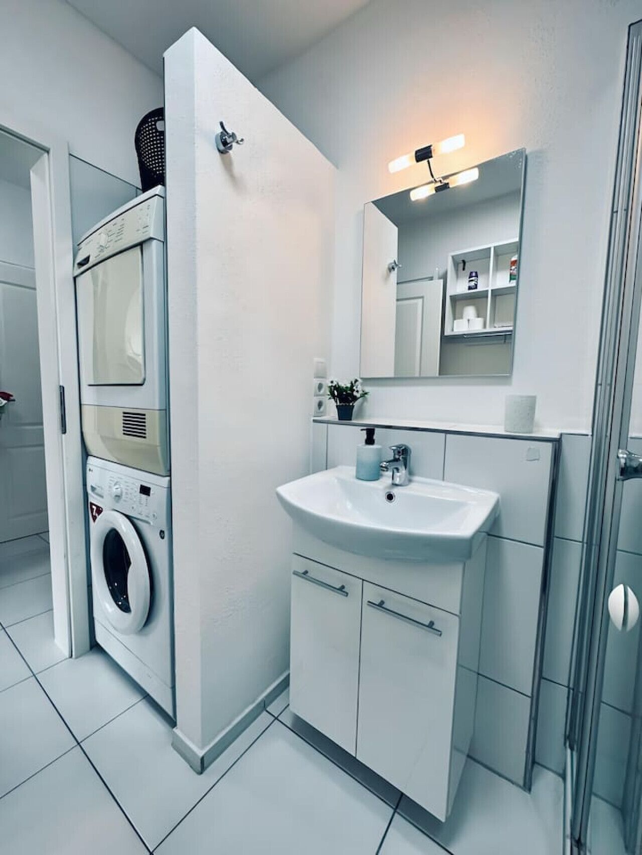 A modern bathroom with a built-in washing machine, a sink, and a mirror with lights.