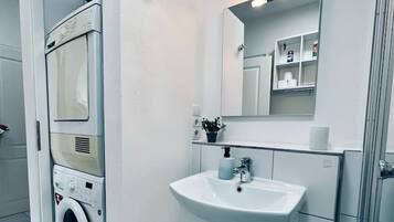 A modern bathroom with a built-in washing machine, a sink, and a mirror with lights.