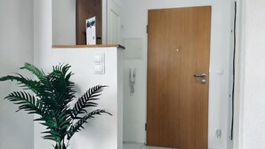 Un passadís amb una porta de fusta, una planta en test i una estant fixada a la paret.
