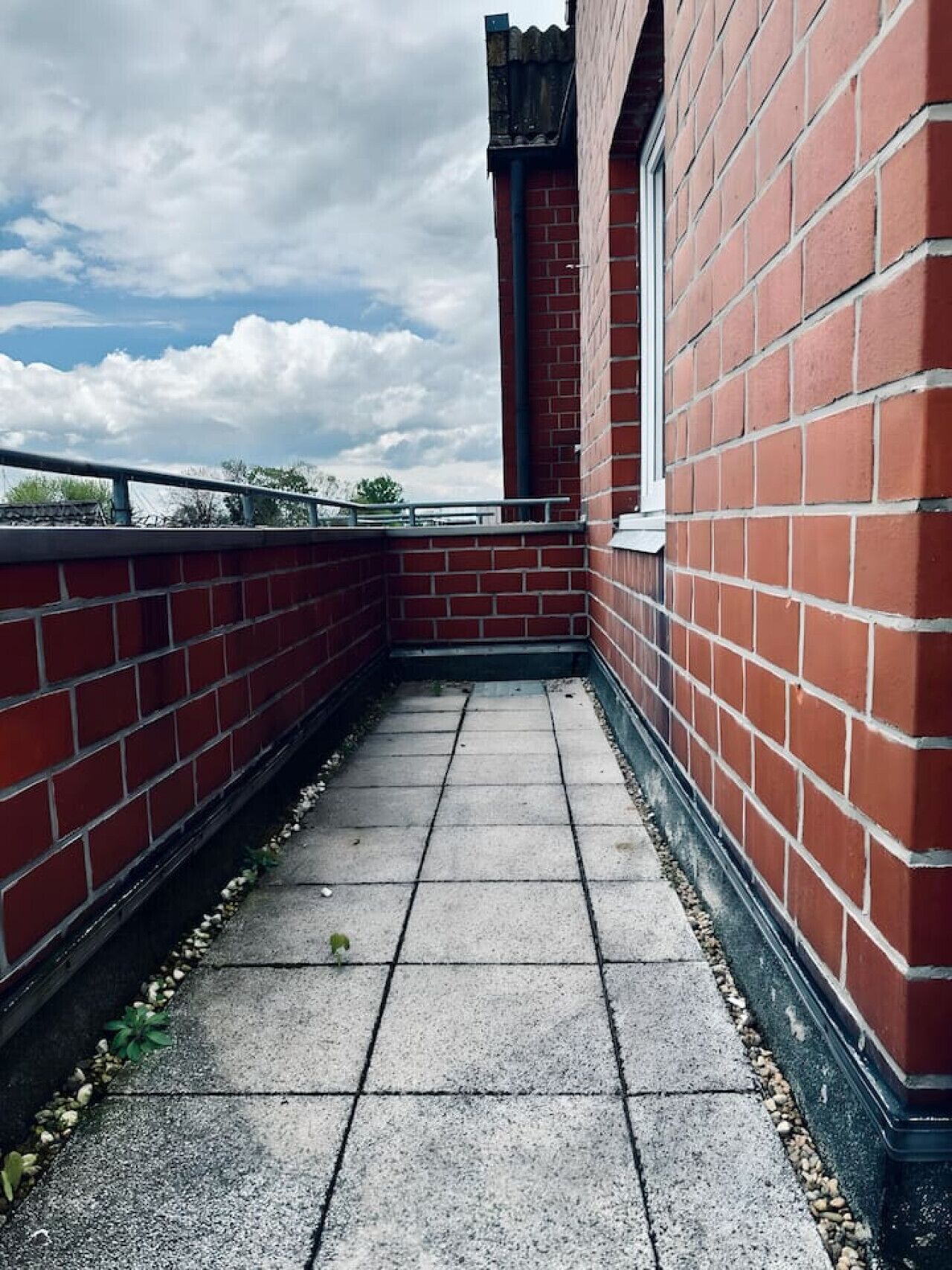 Een smal betonnen pad, begrensd door rode bakstenen muren, dat naar de ingang van een gebouw leidt.