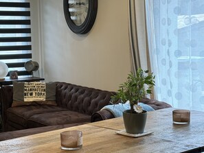 A living room with a brown leather sofa, a wooden coffee table, a potted plant, and a wall clock.