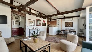 A spacious living area with exposed wooden beams, a dining table, and a kitchen in the background.