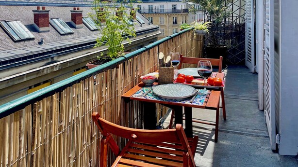 A balcony with a table set for two, a chair, and a potted plant.