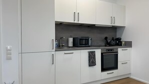 Een moderne keuken met witte kastjes, een magnetron, een waterkoker en een oven.