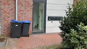 Een modern gebouw met een bakstenen gevel, een glazen ingang en een kleine tuin met een struik.