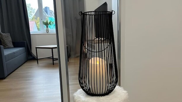 Een moderne woonkamer met een witte, zachte poef, een zwarte metalen stoel en een uitzicht op een stadsbeeld door grote ramen.