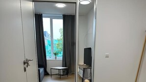 Een moderne, minimalistische kamer met houten vloer, een klein tafeltje, een televisie op een standaard en een raam met gordijnen.