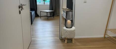 A modern, minimalist room with a wooden floor, a small table, a TV on a stand, and a window with curtains.