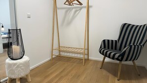 Een kamer met een houten vloer, een gestreept fauteuil, een hangende houten kapstok en een klein krukje met een zwart metalen stoel.