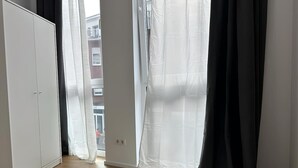 Ein Schlafzimmer mit Bett, Kleiderschrank und Blick durch ein Fenster mit durchsichtigen Vorhängen.