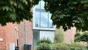 Ein Ziegelweg führt zu einem modernen Gebäude mit großen Fenstern und einer Glasfassade.