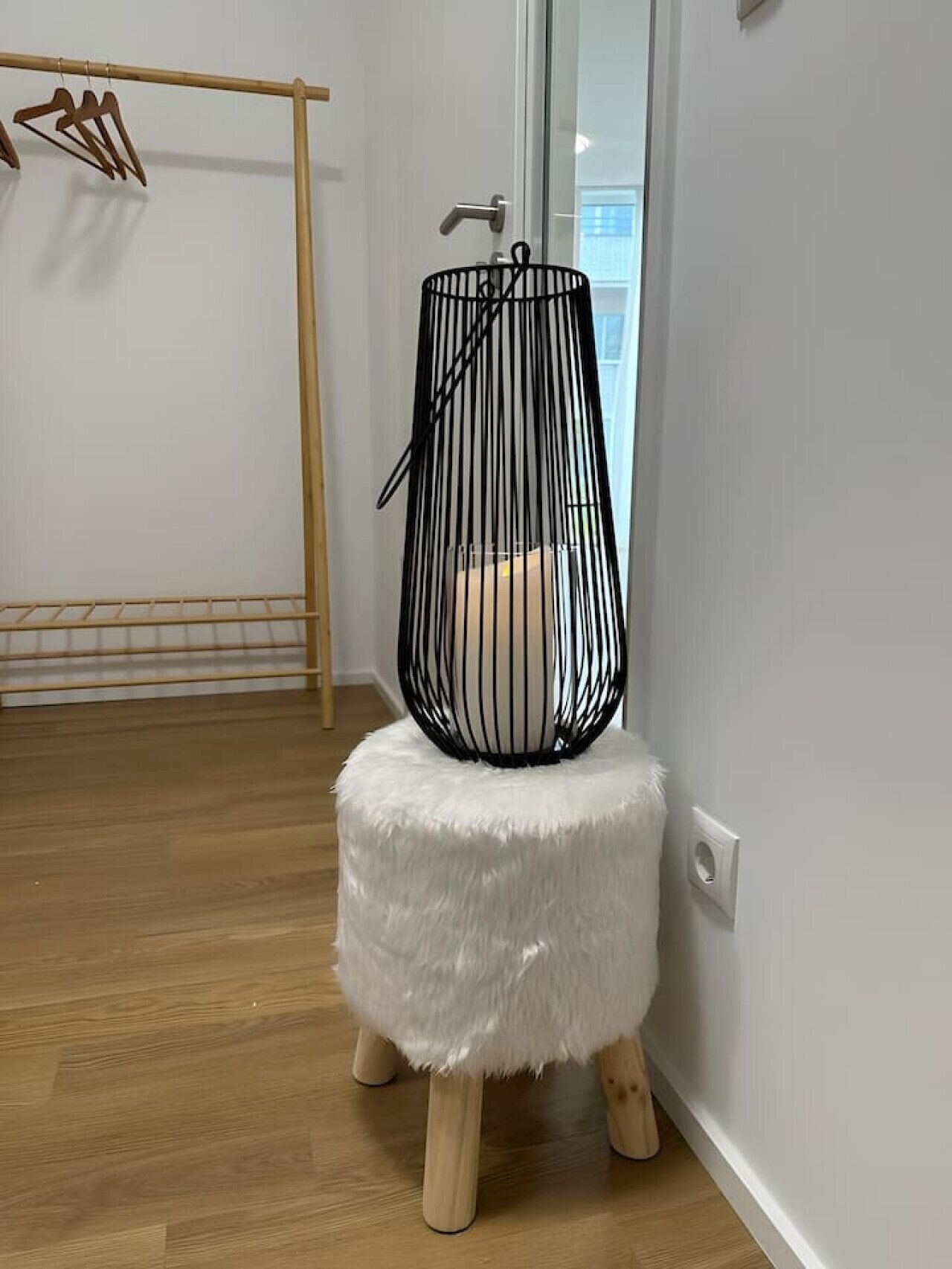 A room with a wooden floor, a white wall, and a black metal object on a white stool.