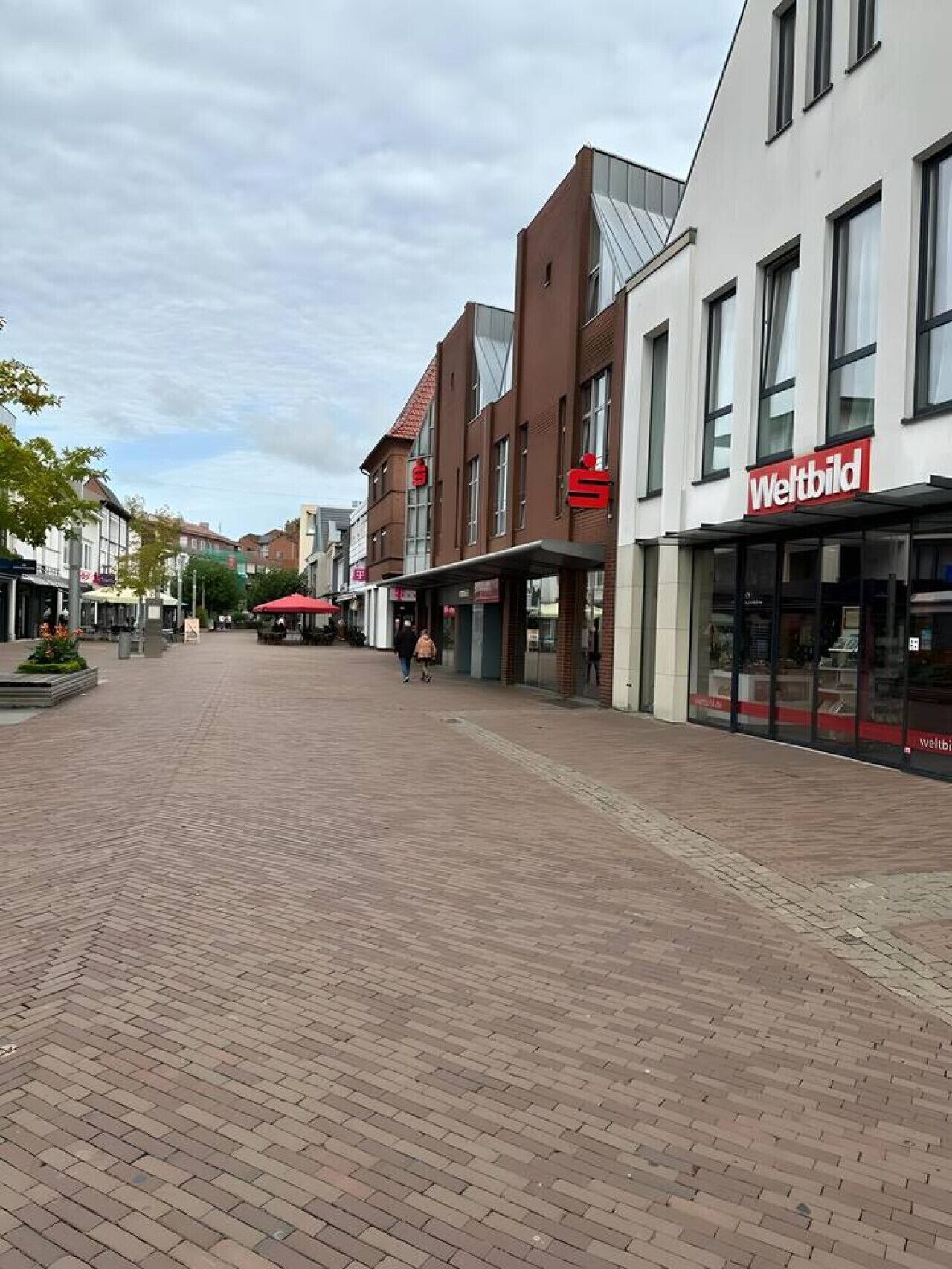A pedestrian street with shops, including a 'Weltbild' store.