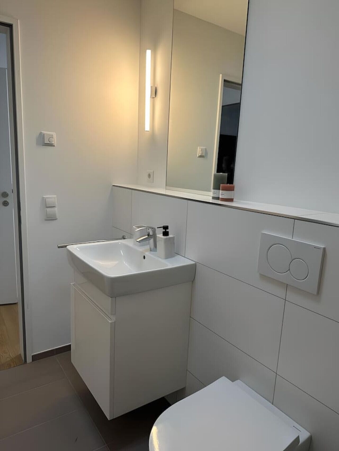 A modern bathroom with a white sink, mirror, and toilet.