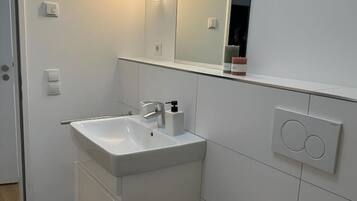 A modern bathroom with a white sink, mirror, and toilet.