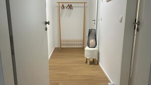 Ein Flur mit Holzboden, einem Kleiderständer, einem kleinen Hocker und einem gerahmten Bild an der Wand.