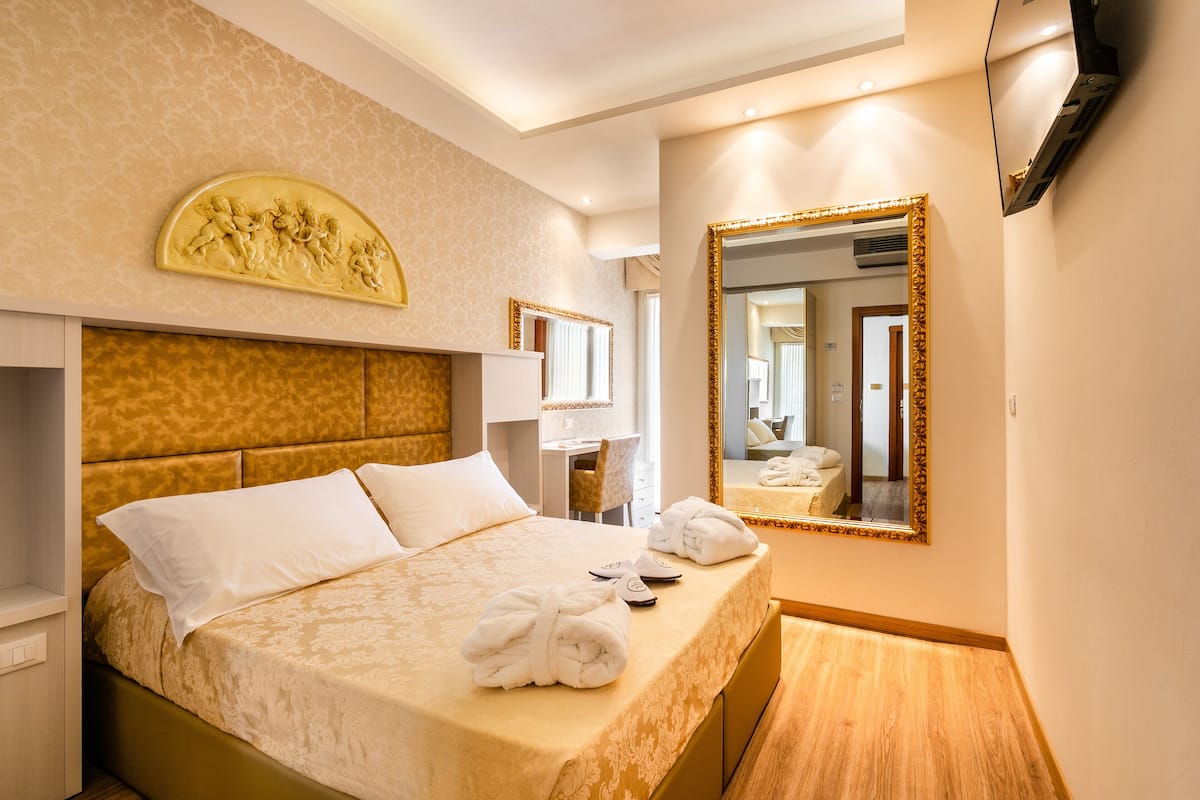 A hotel room with a bed, a desk, a chair, a TV, and a mirror.