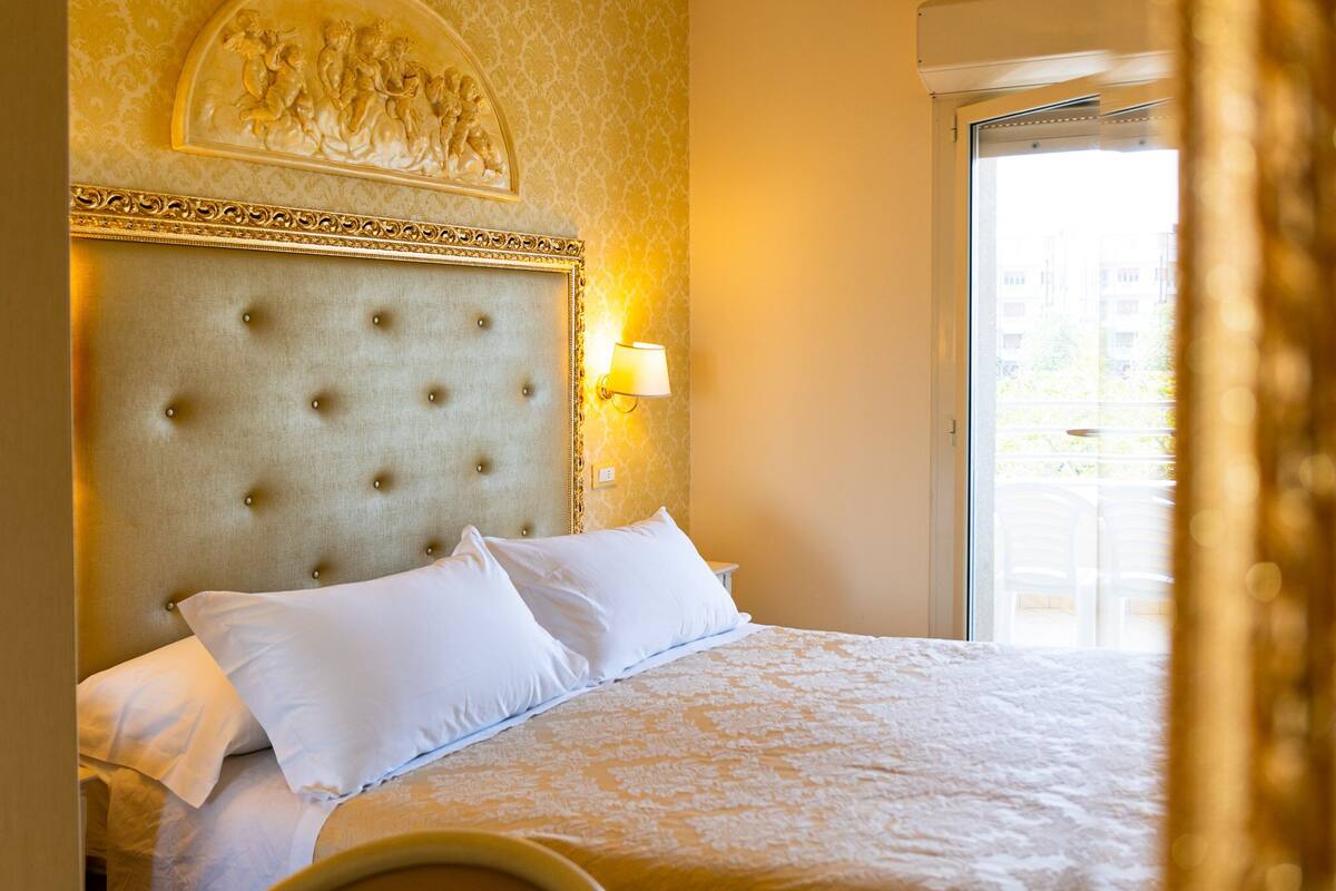 A hotel room with a tufted headboard, white bedding, and a wall-mounted lamp.