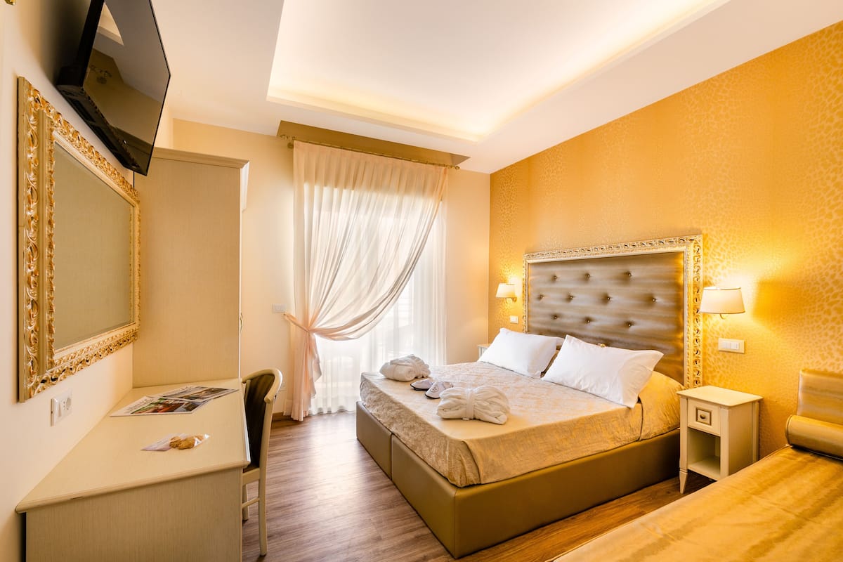 A hotel room with a large bed, bedside tables, a desk, and a television.