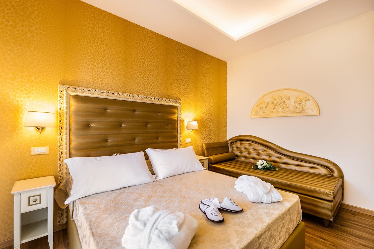 A hotel room with a large bed, a nightstand, a sofa, and a wall-mounted artwork.