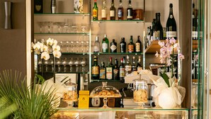 Una zona de bar con estantes llenos de botellas y vasos, una vitrina con pasteles, y un piso de madera.