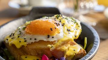 A breakfast dish with poached eggs, hollandaise sauce, and seeds on toast, served in a bowl on a wooden table.