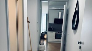 A hallway with wooden flooring, a kitchen area with white cabinets, and a door with a black handle. - Absolute Bestlage Wohnung Artic I (Nordhorn)