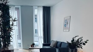 A modern living room with a wooden dining table, black chairs, a sofa, and a potted plant. - Absolute Bestlage Wohnung Artic I (Nordhorn)