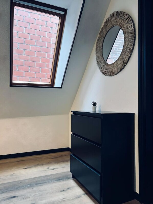 A room with a skylight, a round mirror, and a black dresser.
