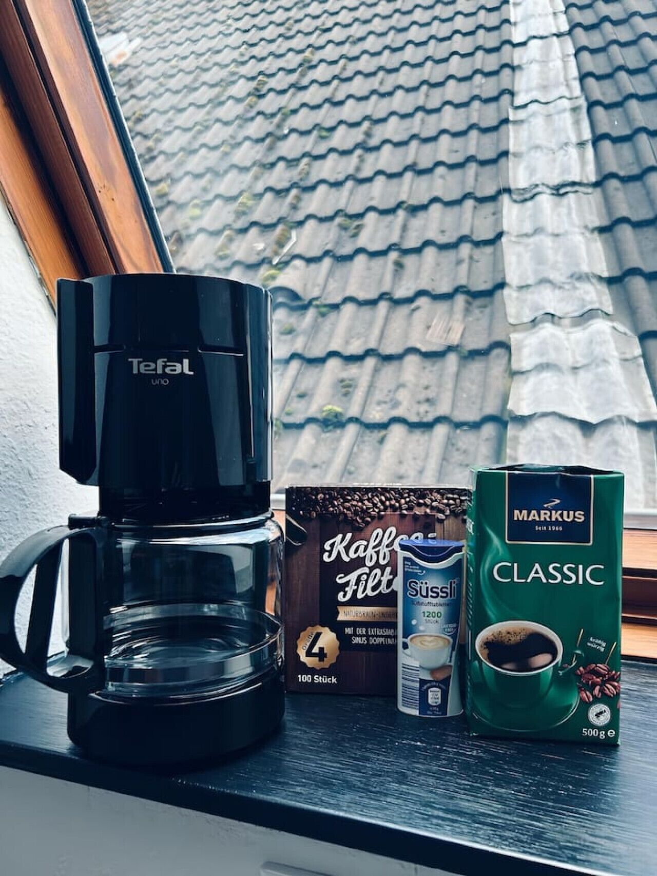 Een koffiezetapparaat, een doos koffiebonen en een koffiekapsule op een vensterbank.