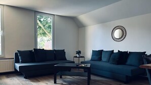 A modern living room with two dark sofas, a coffee table, and a large window providing natural light.