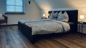 A bedroom with a bed, bedside tables, a chair, a window with blinds, and a wall-mounted decoration.
