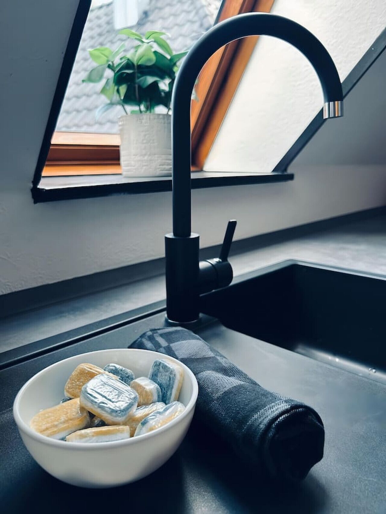 Moderni keittiö, jossa on musta hana, kulho täynnä pientä purtavaa ja ruukkukasvi ikkunalaudalla.