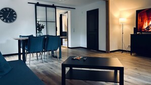 A modern living room with a sofa, dining table, chairs, a coffee table, a clock, a sliding door, a fireplace, and a TV.