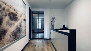 A hallway with wooden flooring, a black railing, and a large abstract painting on the left wall.