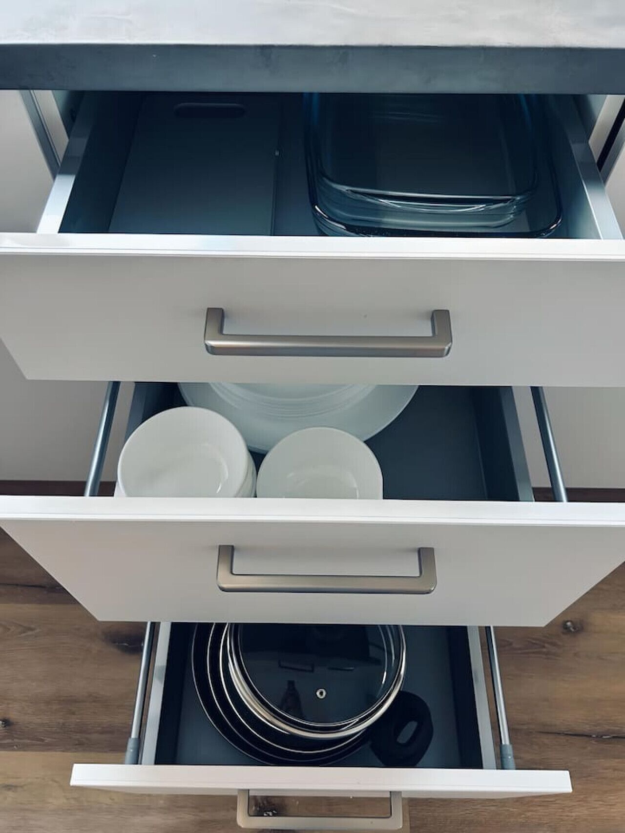 A drawer with white handles containing white plates and a black circular object.